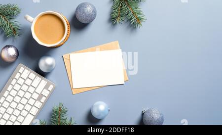 Christmas card mockup, cup of coffee, keyboard, Xmas decorations, balls, pine branches on pastel blue background. Modern home office desk table. Chris Stock Photo