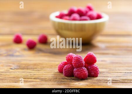 Fresh respberries lying on wooden table with full bowl in background. Stock Photo