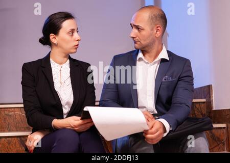 Employees on staircase late night afterhours tired from overtime, busy man and woman dealing with overwork and deadline. Colleague entrepreneur working late together in evening at corporate job sitting on staircase, explaining difficult finance project. Stock Photo