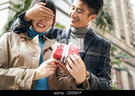 young asian man giving girlfriend a surprise present outdoors Stock Photo