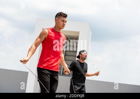 Two handsome Caucasian sportsmen doing morning outdoor jumping rope exercise on outdoor rooftop Stock Photo