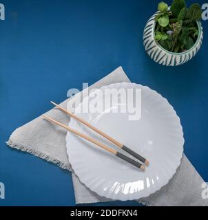 On the table on a napkin is an empty white plate with wooden chopsticks on it. Sample of Japanese cuisine. The view from the top, flat lay Stock Photo