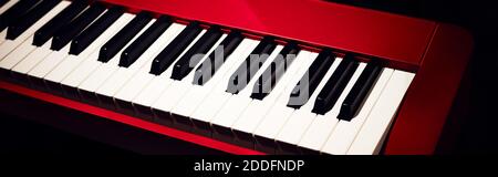 Electronic synthesizer (piano keyboard) close-up shot with dark background. Beautiful red musical keyboard with balck and white keys. Stock Photo