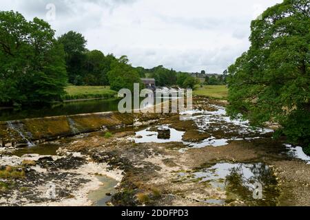River Wharfe & weir in scenic countryside - low shallow water in dry weather, rocks on exposed riverbed - Grassington, North Yorkshire, England, UK. Stock Photo