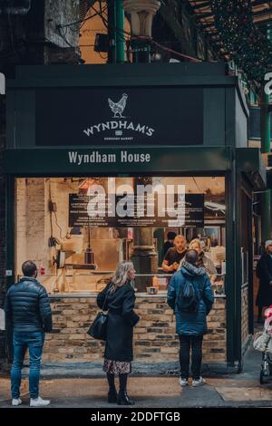 London, UK - November 19, 2020: People socially distanced queuing at a Wyndham take away food stall in Borough Market, one of the largest and oldest f Stock Photo