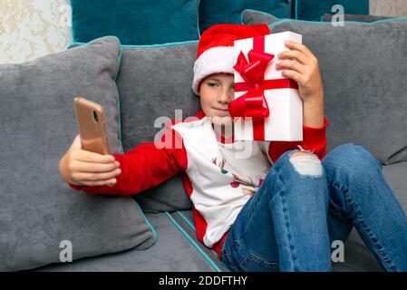 Handsome kid in Santa Claus hat looks at smartphone screen, shows a christmas present.Talk with family,closeup image. Stock Photo