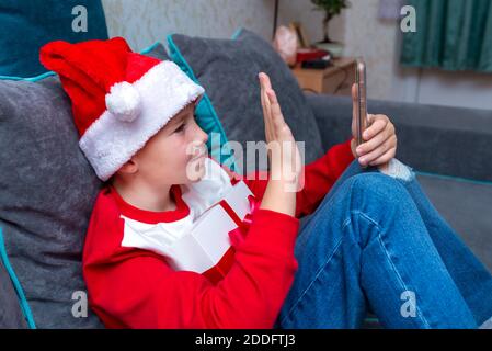 Handsome boy in Santa Claus hat looks at smartphone screen, greeting friends.Talk with family,closeup side view image. Stock Photo