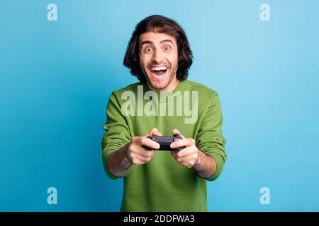 Photo of excited gamer guy hold controller amazed open mouth wear green sweater isolated blue color background Stock Photo