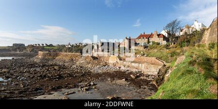 The tide is out at Crail exposing the very rocky coastline, that is so good for rock pooling. At higher tides the waves smash against the sea wall. Stock Photo