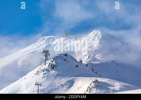 Empty ski lift heading toward the top of the snow-capped mountain lost in the cloud. Stock Photo