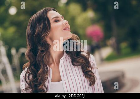 Side profile photo portrait of nice girl with curly hair breathing fresh air in city park wearing striped white shirt Stock Photo