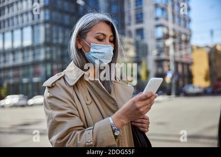 Elegant woman in medical mask using cellphone on the street Stock Photo