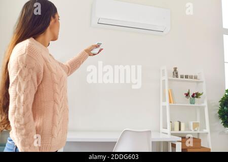 Young woman standing in living-room and switching on air conditioner with remote control Stock Photo