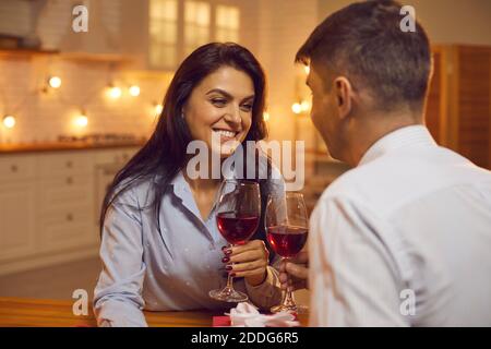 Beautiful young woman drinking red wine with her lover sitting in the kitchen at home. Stock Photo