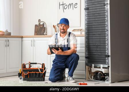 Worker repairing fridge in kitchen Stock Photo