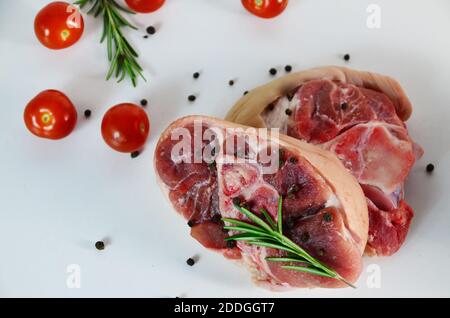 pieces of raw pork steaks, with ingredients for cooking, served on woodenboard. with rosemary, cherry tomatoes, black pepper and olive oil on the tabl Stock Photo