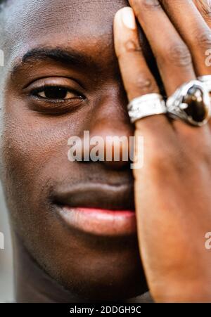 Handsome African American male with trendy rings on fingers touching face and smiling at camera Stock Photo