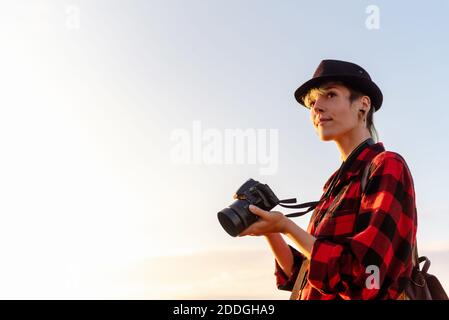 Side view of androgynous female traveler with professional photo camera standing on hill in mountainous area Stock Photo