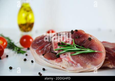 pieces of raw pork steaks, with ingredients for cooking, served on woodenboard. with rosemary, cherry tomatoes, black pepper and olive oil on the tabl Stock Photo