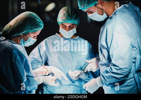 Group of focused professional surgeons with surgical tools and thread finishing operation of patient in operating theater Stock Photo