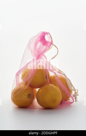 Still life with lemons in pink net textile bag backlit on white background Stock Photo
