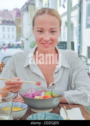 Woman eating tasty colorful healthy natural organic vegetarian Hawaiian poke bowl using asian chopsticks on rustic wooden table. Healthy natural Stock Photo