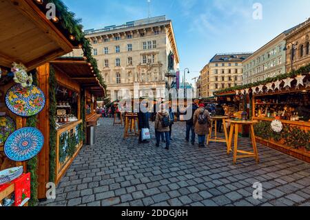 People walking among wooden kiosks on cobblestone street selling gifts and souvenirs during famous traditional Christmas market in Vienna, Austria. Stock Photo
