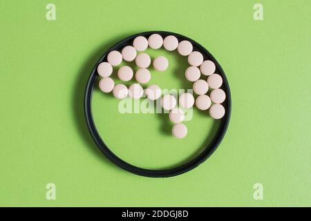 A brain made up of small round pills inside a circular lens on a green table. Health concept. Stock Photo