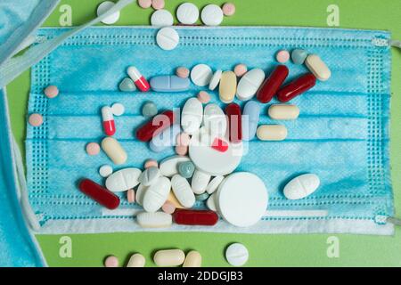 Piles of drugs scattered on a surgical mask and a green table. Personal protective equipment covered by various medications. Stock Photo