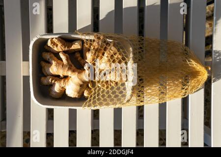Top view of fresh ginger roots in paper container placed on wooden table on sunny day Stock Photo