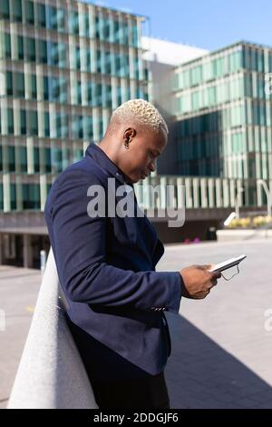 Side view of smiling African American businessman standing in downtown and browsing tablet online Stock Photo