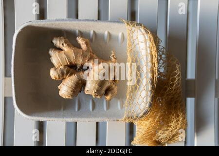 Top view of fresh ginger roots in paper container placed on wooden table on sunny day Stock Photo