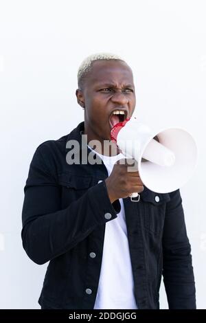 African American male shouting in loudspeaker while standing on white background Stock Photo