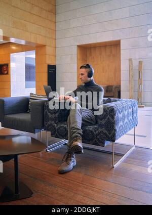 Young focused businessman in headphones having video call via netbook at hotel lobby Stock Photo