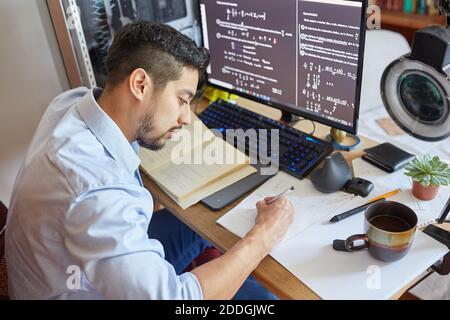 Side view high angle of crop male student sitting at table and writing on sheet of paper and preparing for exam Stock Photo