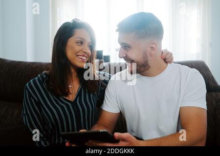 Couple browsing tablet computer and looking at each other smiling while entertaining at weekend Stock Photo