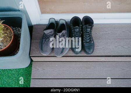From above of male sneakers and female leather boots placed on wooden step at doorway of cabin Stock Photo
