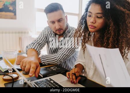 High angle of content multiracial couple of entrepreneurs sitting at table and reading paper documents while working from home Stock Photo
