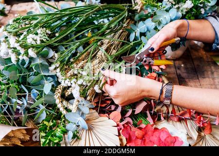 From above cropped unrecognziable professional female florist arranging flower bouquet while working in shop on wooden table Stock Photo