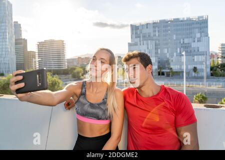 Young slim Woman n sportswear and strong muscular man taking selfie on smartphone after fitness workout together in city Stock Photo