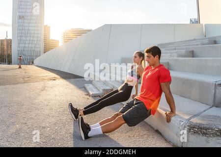 Full body side view of determined young active man and Woman in sportswear doing reverse push ups against concrete steps during fitness workout togeth Stock Photo