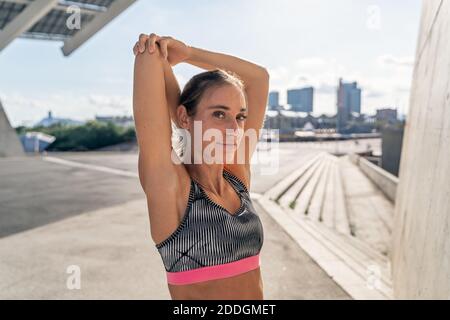 Charming female runner stretching arms while warming up before training and looking at camera Stock Photo