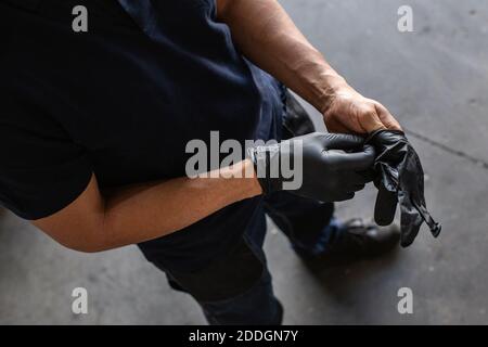 From above anonymous male employee putting on latex gloves during work in garage Stock Photo