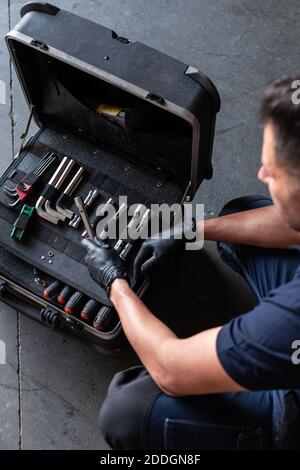 From above male technician picking screwdriver bits from tool box while working in garage Stock Photo