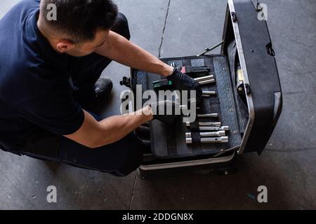From above male technician picking screwdriver bits from tool box while working in garage Stock Photo