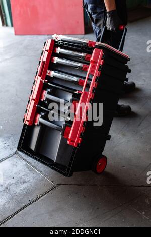 High angle of anonymous technician walking and pulling modern tool box during work in professional workshop Stock Photo