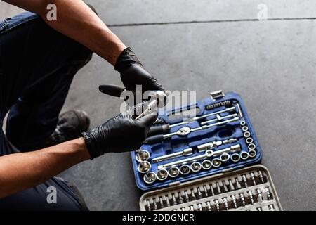 From above anonymous male technician in latex gloves selecting wrench bit from tool box during work in garage Stock Photo