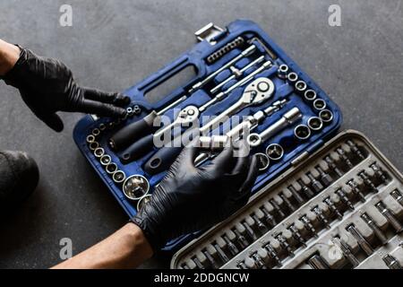 From above anonymous male technician in latex gloves selecting wrench bit from tool box during work in garage Stock Photo