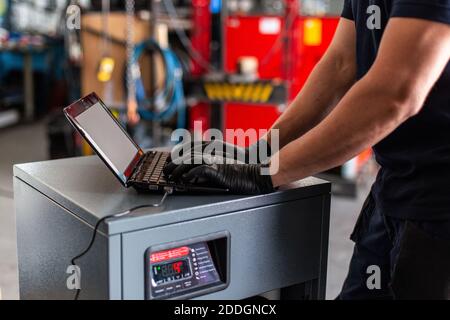 Adult man in using laptop to program broken machine during work in modern workshop Stock Photo