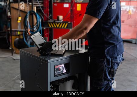 Unrecognizable adult man in using laptop to program broken machine during work in modern workshop Stock Photo